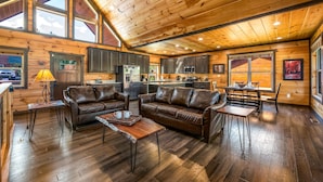 A spacious cabin interior with a wooden ceiling, large windows, a kitchen, and leather seating.