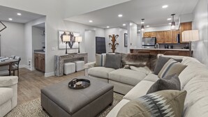 Ein modernes Wohnzimmer mit Ecksofa, Hocker und einem Essbereich mit Tisch und Stühlen.