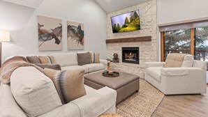 Ein modernes Wohnzimmer mit Kamin aus Stein, einem großen Flachbildfernseher und einer gemütlichen Sitzecke mit Sofa und Sesseln.