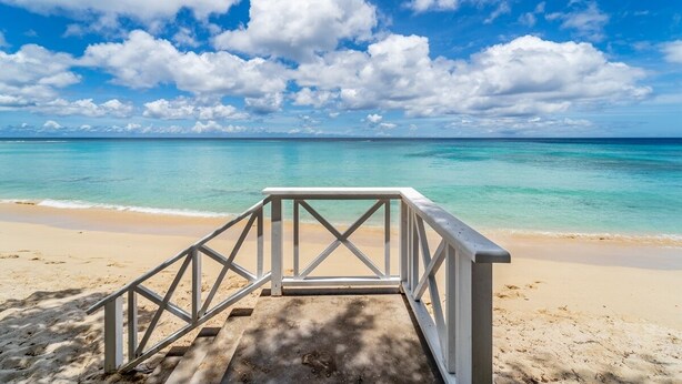 Ein Strand mit einer Holzstege, der zum Wasser führt, unter blauem Himmel und ruhiger See.