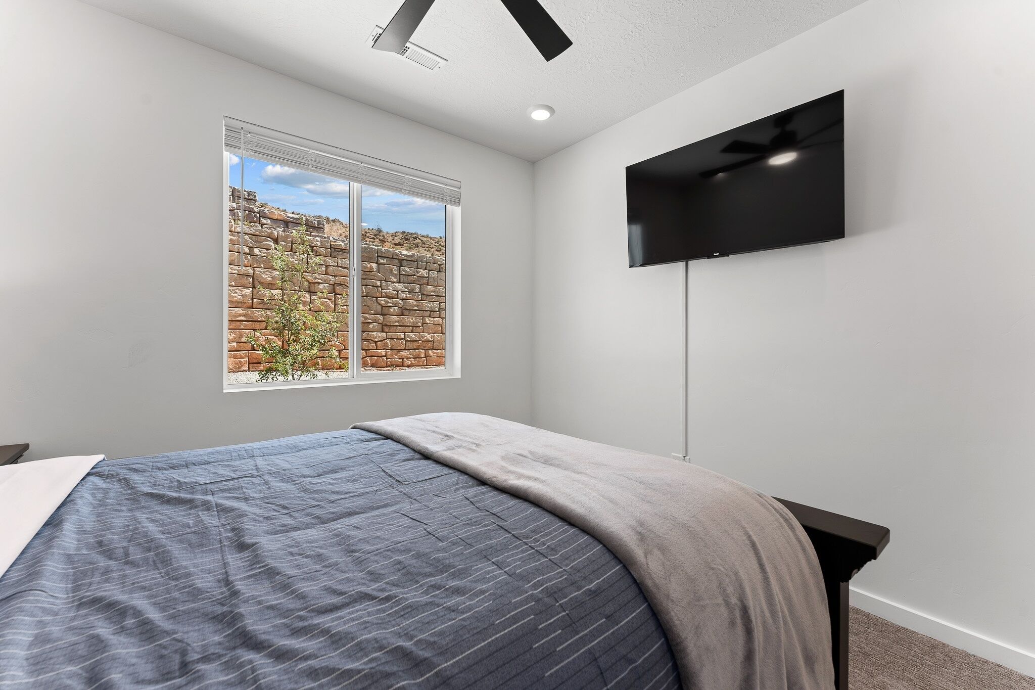 Une chambre à coucher avec un lit, un téléviseur fixé au mur et une fenêtre donnant sur un mur en briques.