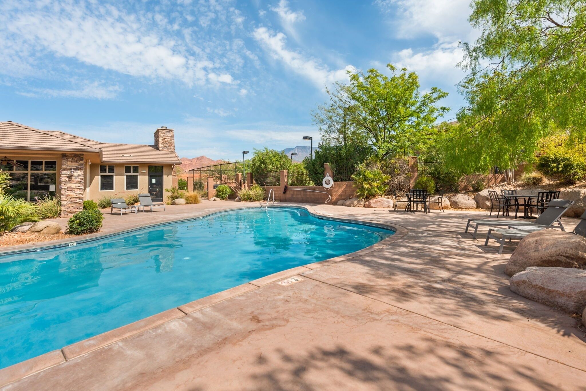 A swimming pool with a stone facade building in the background, surrounded by greenery and outdoor furniture.