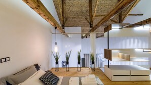 A modern room with exposed wooden beams, a sofa with cushions, a bedside table, a lamp, and a built-in shelving unit. - Aigli Seafront Loft-bespoke Design Gem (Kalamata)
