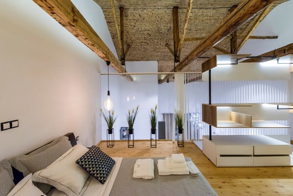 Une chambre moderne avec des poutres apparentes, un canapé avec des coussins, une table de chevet, une lampe et une bibliothèque intégrée.