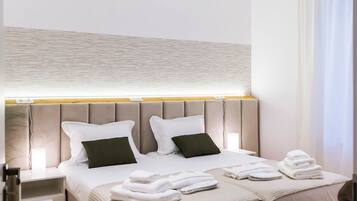 A modern hotel room with a large bed, a bedside table, and a headboard with integrated lighting.