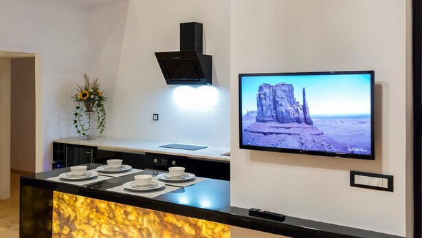 A modern kitchen with a marble countertop, a black range hood, and a flat-screen TV displaying a desert landscape. - Aigli Seafront Loft-bespoke Design Gem (Kalamata)