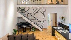 A modern interior with a wooden ceiling, a staircase with geometric wall art, a piano, a sofa, a dining area, and a hanging light fixture. - Aigli Seafront Loft-bespoke Design Gem (Kalamata)