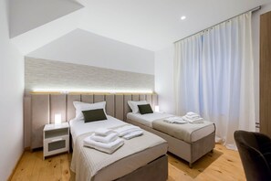 Une chambre d’hôtel moderne avec deux lits, une table de chevet, une chaise et une grande fenêtre avec des rideaux.