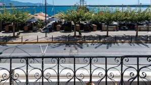 A balcony with potted plants, a clear view of the sea, and a distant marina with boats. - Aigli Seafront Loft-bespoke Design Gem (Kalamata)