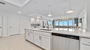 Une cuisine spacieuse avec des meubles blancs, un grand îlot central doté d’un évier et un éclairage suspendu.