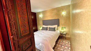 A bedroom with a large bed, a patterned headboard, two wall-mounted lights, and a small bedside table with a lamp. - Charming Riad la perle des Oudayas - Rabat (Rabat)