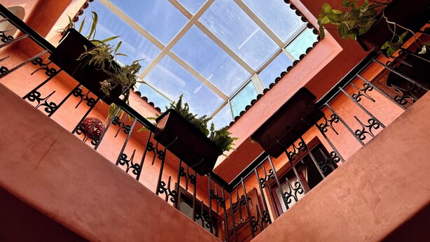 A view of a building's interior with a large window, metal railings, and potted plants. - Charming Riad la perle des Oudayas - Rabat (Rabat)