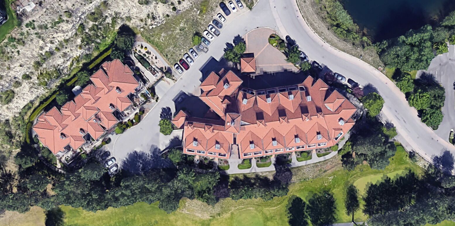 An aerial view of a residential area with multiple houses, a parking lot, and a curved road.