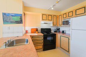 A kitchen with wooden cabinets, a stainless steel sink, a black stove, and a microwave. - Classic Loft - 309 (Kelowna)