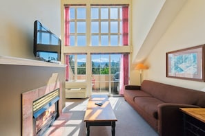 A living room with a fireplace, a television, a sofa, a table, and a balcony with a view.