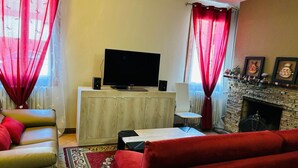 A living room with a flat-screen TV, speakers, a fireplace, and red curtains.
