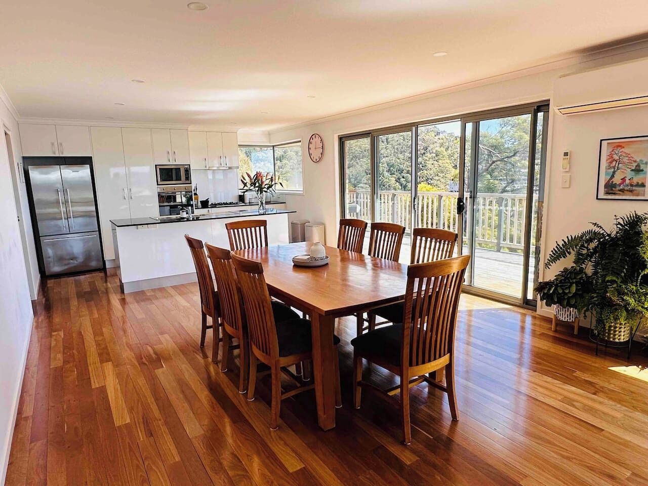 A modern kitchen with white cabinets, a stainless steel refrigerator, and a dining area with a wooden table and chairs.