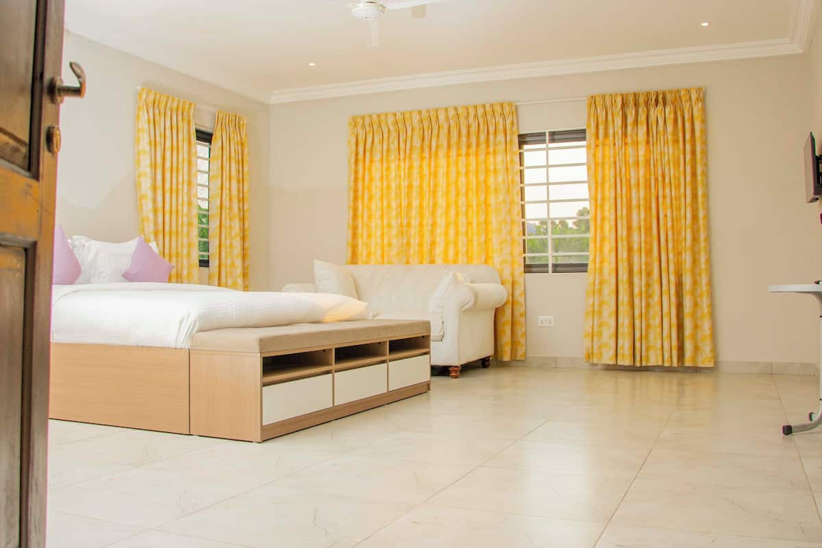 A bedroom with a bed, a sofa, a desk, and curtains.