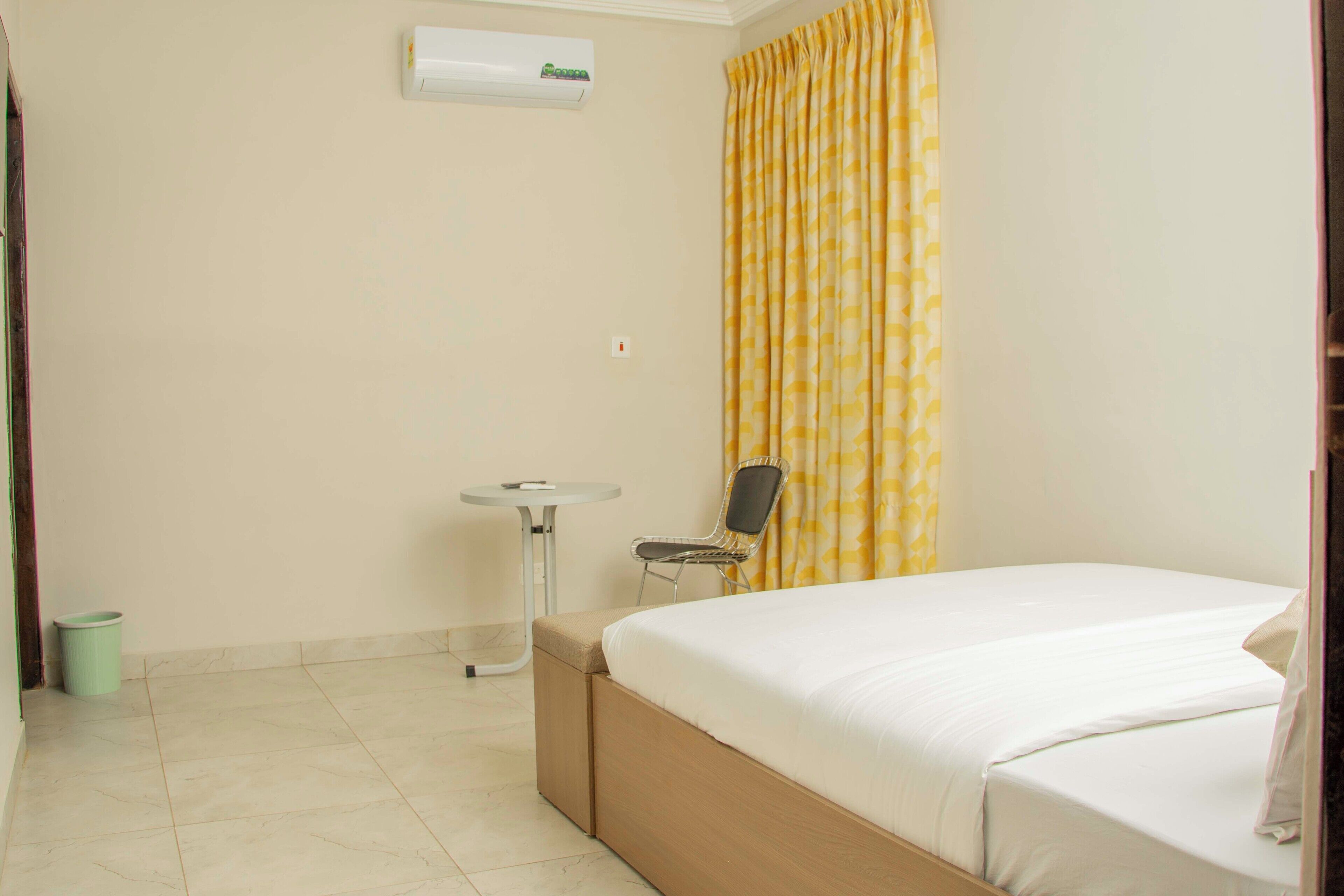 A hotel room with a bed, a small table, a chair, and an air conditioning unit on the wall.