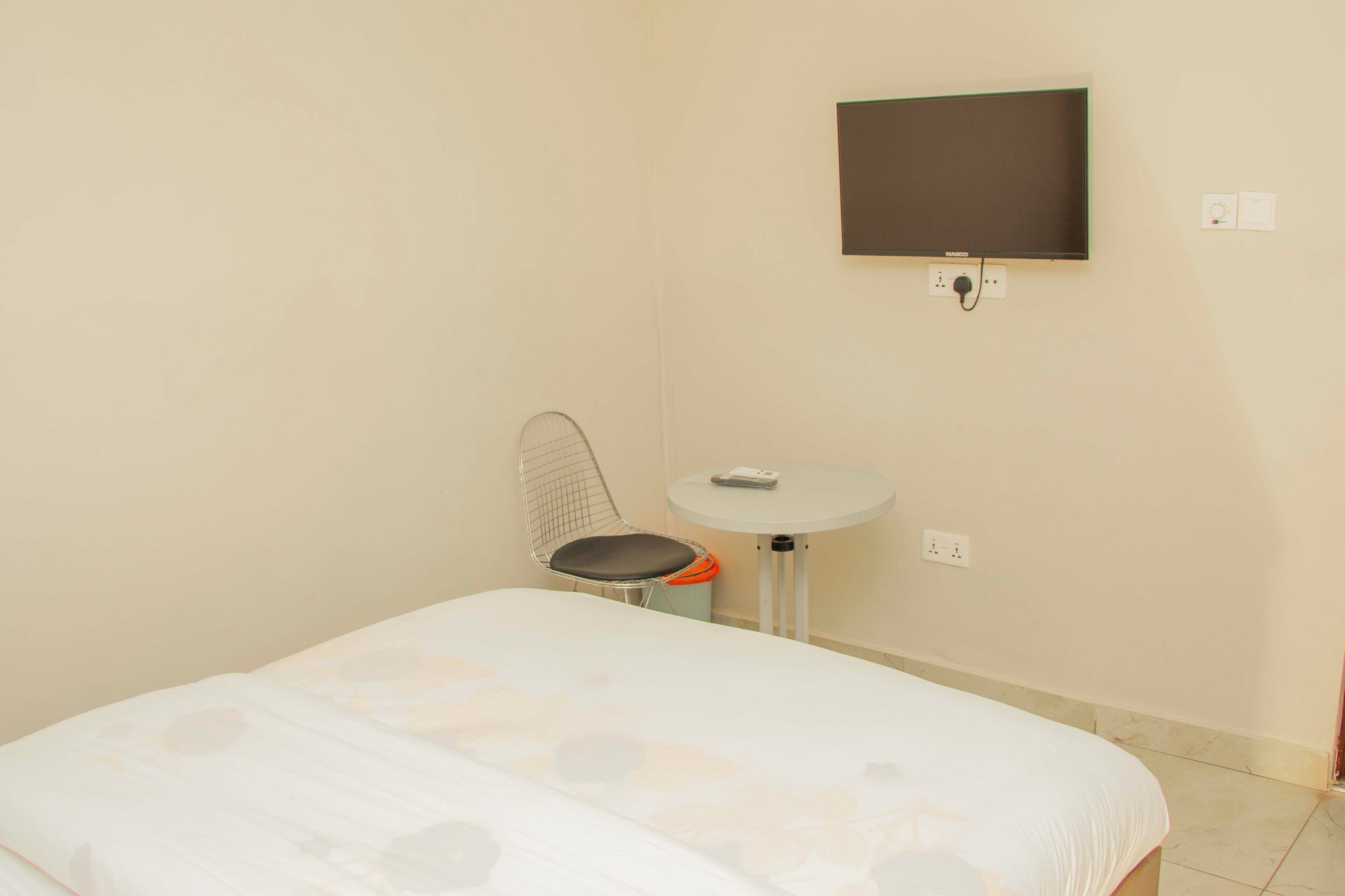 A bedroom with a bed, a chair, a small table, and a wall-mounted TV.