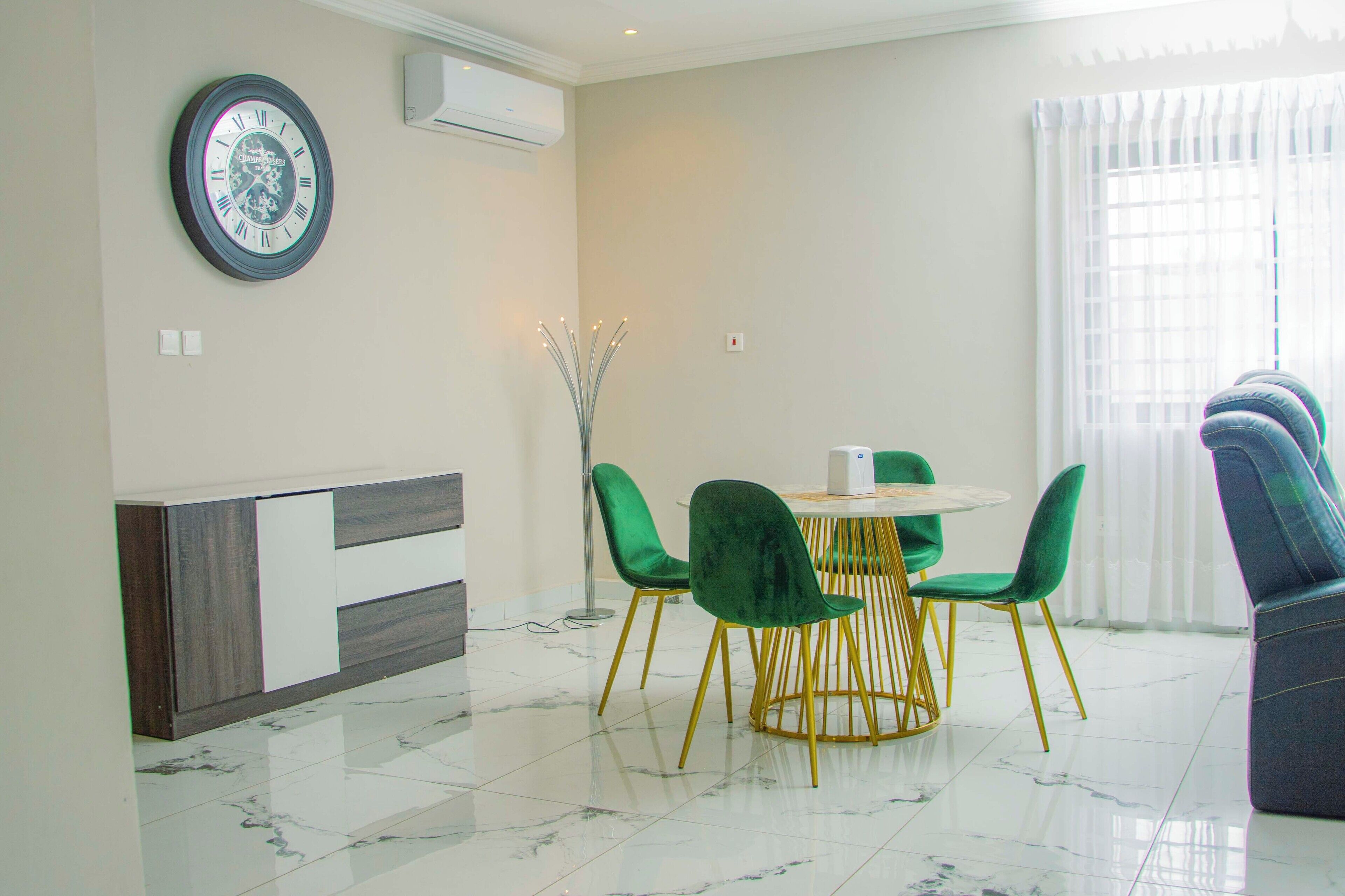 A modern dining area with a round table, green chairs, and a clock on the wall.