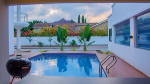 Ein Swimmingpool mit Grill, umgeben von einer weißen Mauer mit Pflanzen und Blick auf Häuser im Hintergrund.