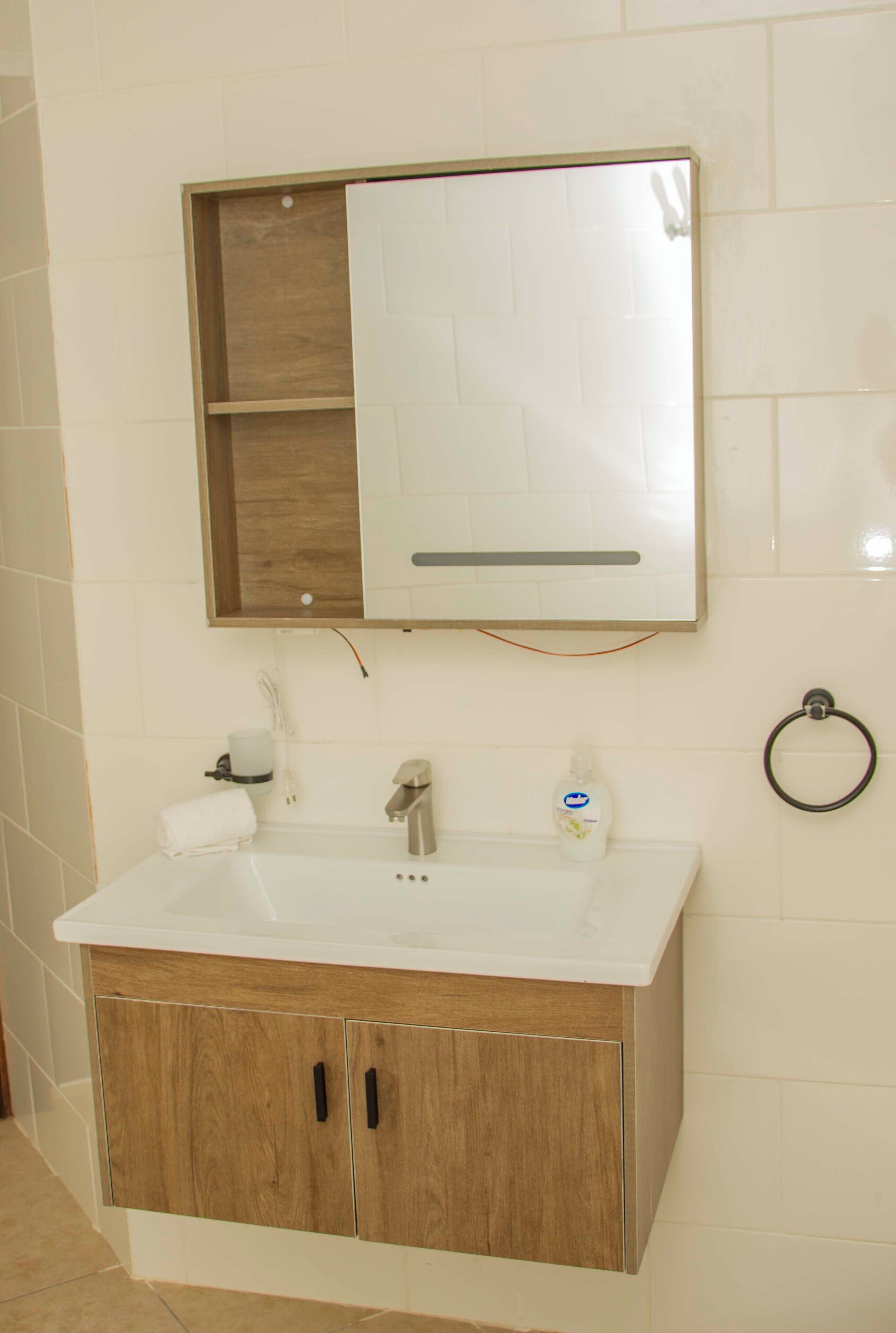 A bathroom with a white sink, wooden cabinet, and a mirror above it.