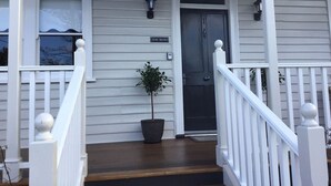 A white house with a front porch, a potted plant, and a door labeled 'THE MANS'. - Cosy Studio, "The Maid" easy walking to City (Sandy Bay)