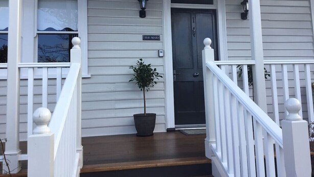 A white house with a front porch, a potted plant, and a door labeled 'THE MANS'.
