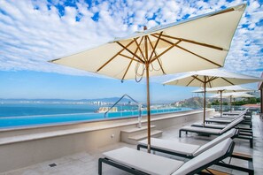 A rooftop terrace with lounge chairs and umbrellas overlooking a pool and cityscape. - Rooftop Pool + BBQ Terrace | Luxury Ocean View 2BR (Puerto Vallarta)