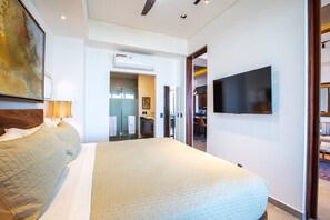 A hotel room with a large bed, a television mounted on the wall, and a bathroom visible through an open door. - Rooftop Pool + BBQ Terrace | Luxury Ocean View 2BR (Puerto Vallarta)