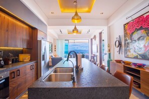 A modern kitchen with a central island, stainless steel appliances, and a view to the outside. - Rooftop Pool + BBQ Terrace | Luxury Ocean View 2BR (Puerto Vallarta)