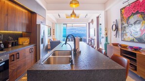 A modern kitchen with a central island, stainless steel appliances, and a view to the outdoors. - Rooftop Pool + BBQ Terrace | Luxury Ocean View 2BR (Puerto Vallarta)