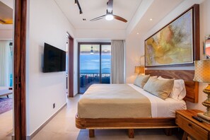 A hotel room with a large bed, a television, a ceiling fan, and a view of the sea. - Rooftop Pool + BBQ Terrace | Luxury Ocean View 2BR (Puerto Vallarta)