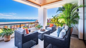A balcony with wicker furniture, a ceiling fan, and a view of the beach. - Rooftop Pool + BBQ Terrace | Luxury Ocean View 2BR (Puerto Vallarta)