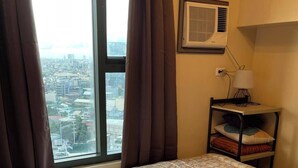 A hotel room with a bed, a nightstand, a lamp, and a window with curtains. - Lovely 1-bedroom condo in fabulous Makati with WiFi, AC, fitness room (Makati)