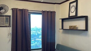 A modern living room with a green sofa, a small round table, a ceiling light fixture, and a window with curtains. - Lovely 1-bedroom condo in fabulous Makati with WiFi, AC, fitness room (Makati)