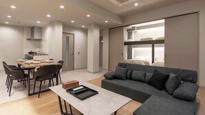A modern living room with a grey sofa, a dining table with chairs, and a kitchen area in the background. - Crice Hotel Shinsaibashi (Osaka)
