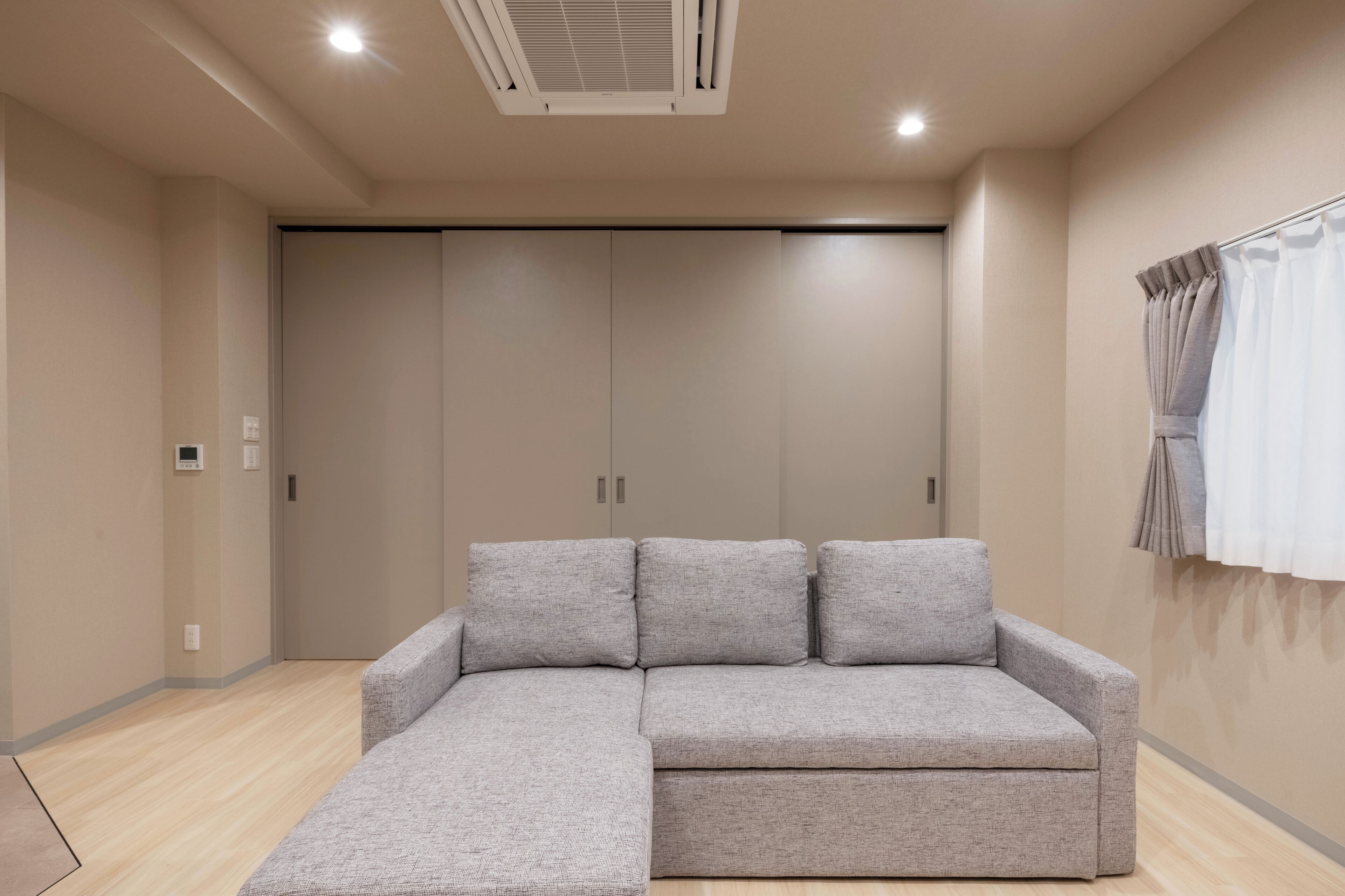A modern room with a grey sectional sofa, a large wardrobe, and a ceiling air conditioner.