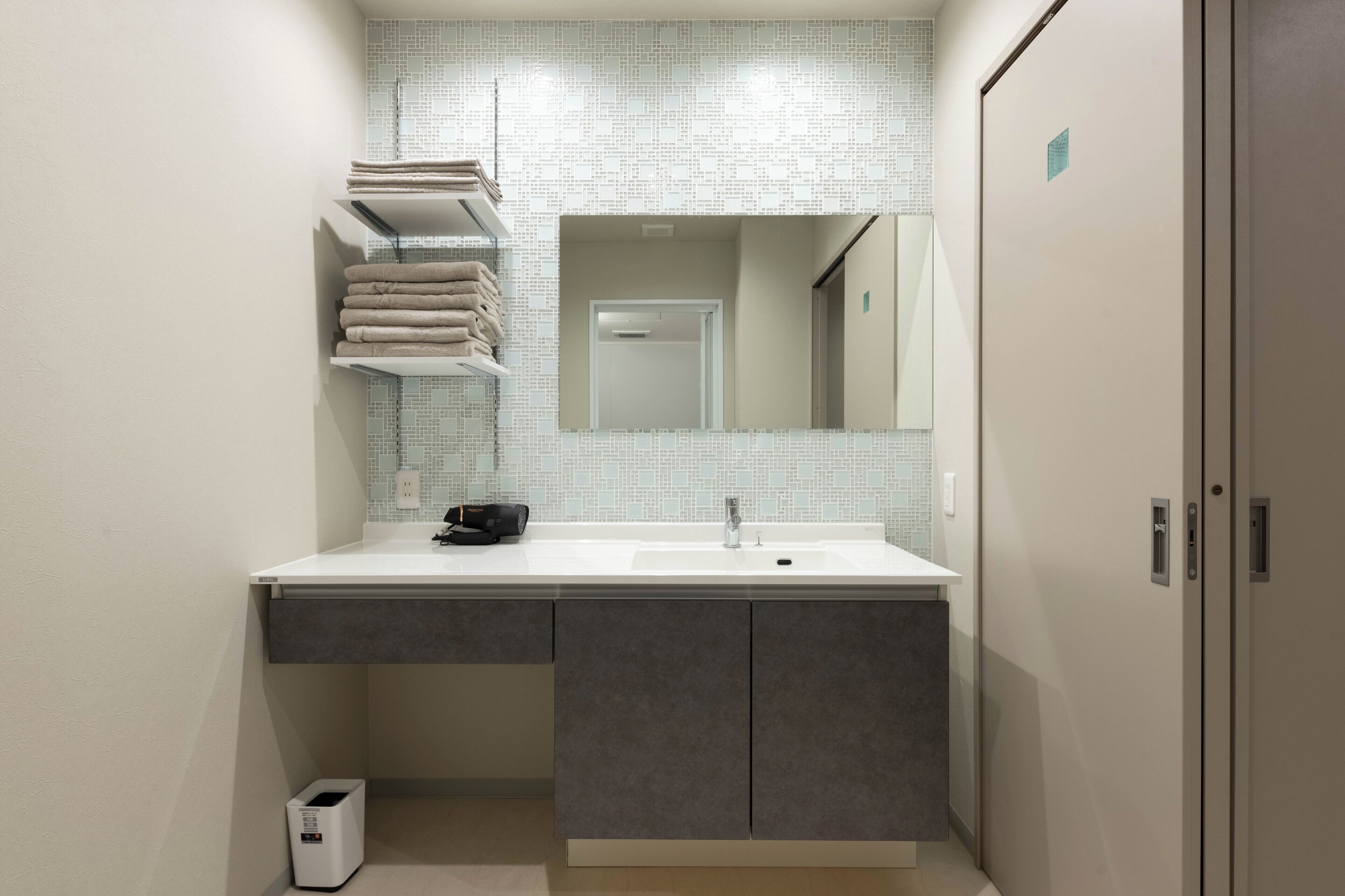 A modern bathroom with a white sink, dark cabinets, and a tiled backsplash.