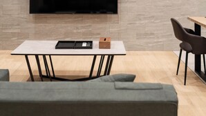 A modern living room with a flat-screen TV mounted on a textured wall, a minimalist table with a tray, and contemporary furniture. - Crice Hotel Shinsaibashi (Osaka)