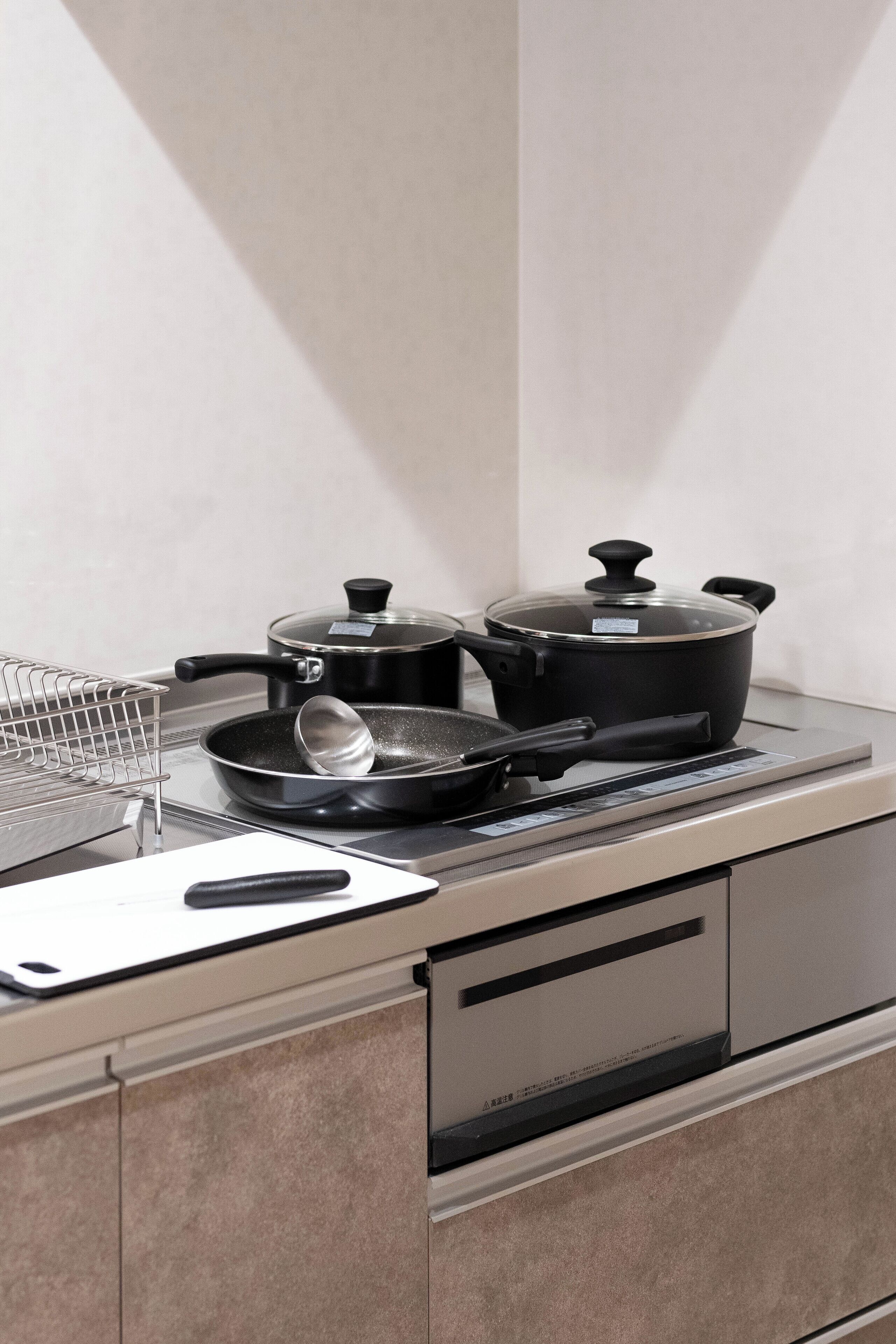 A kitchen with a stove, a frying pan, a pot, and a ladle.