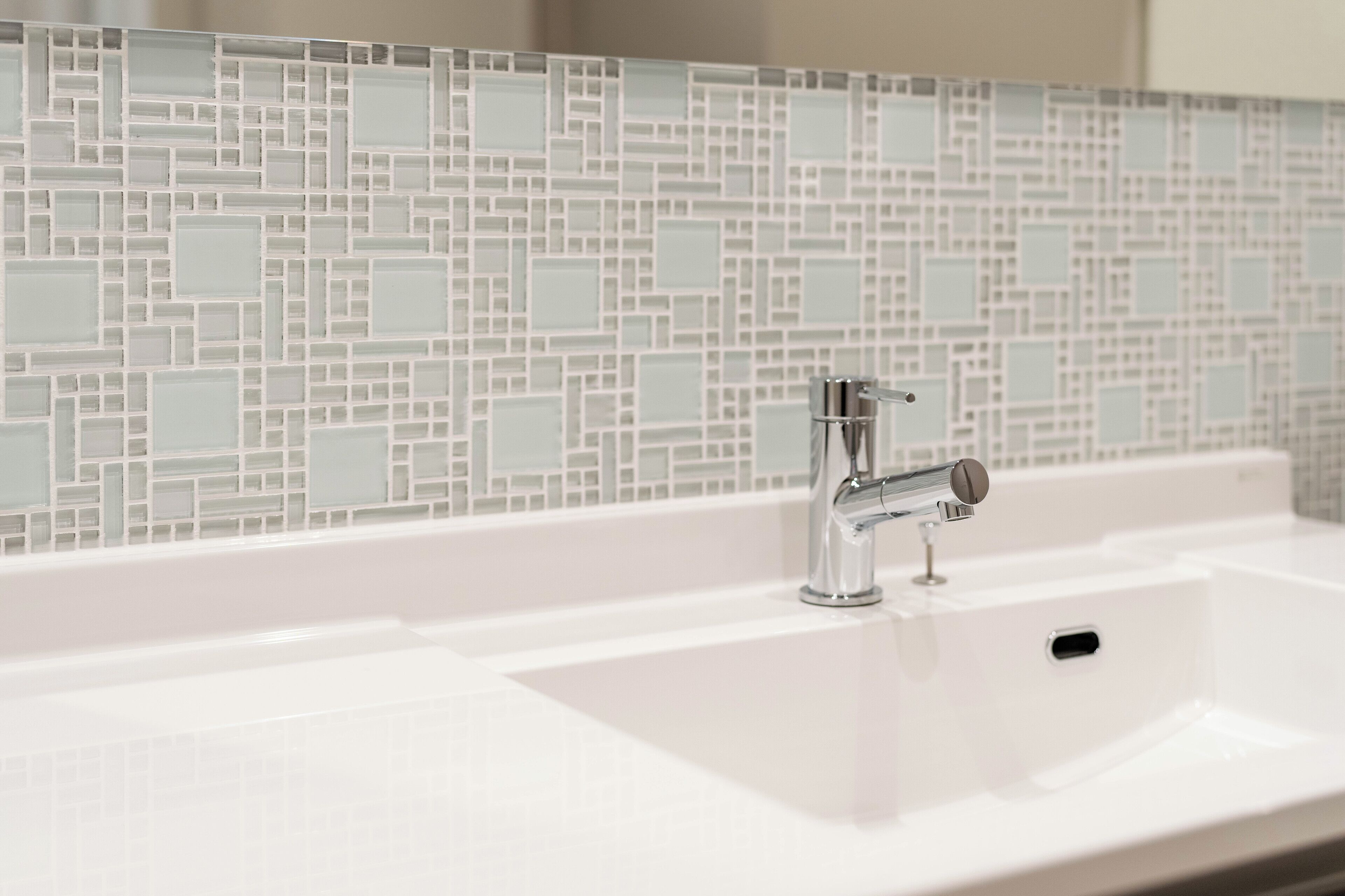 A bathroom with a white sink, chrome faucet, and a tiled backsplash.