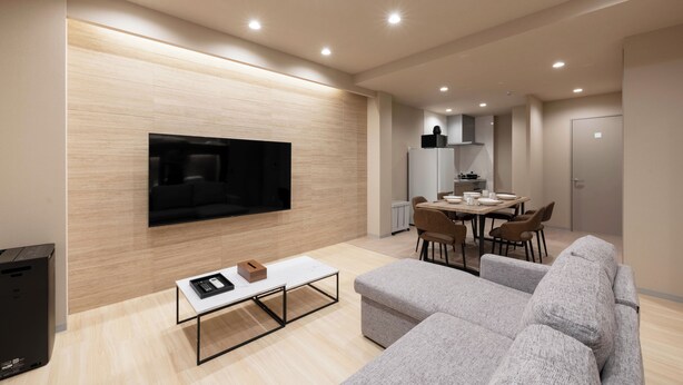 A modern living room with a flat-screen TV, grey sofas, a coffee table, and a dining area with chairs and a table. - Crice Hotel Shinsaibashi (Osaka)