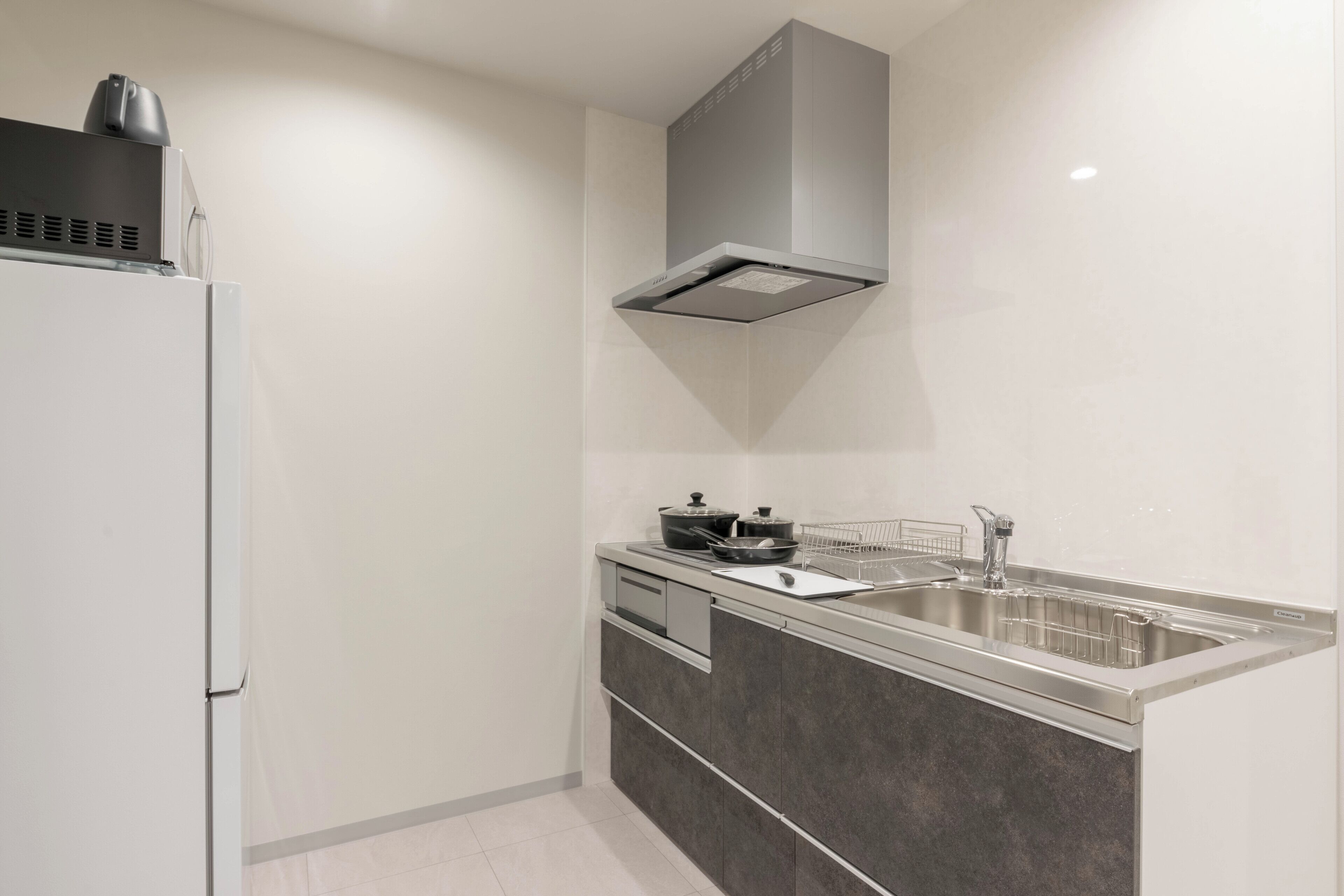 Una cocina moderna con estufa integrada, un lavamanos de acero inoxidable y una campana extractora gris sobre la estufa.