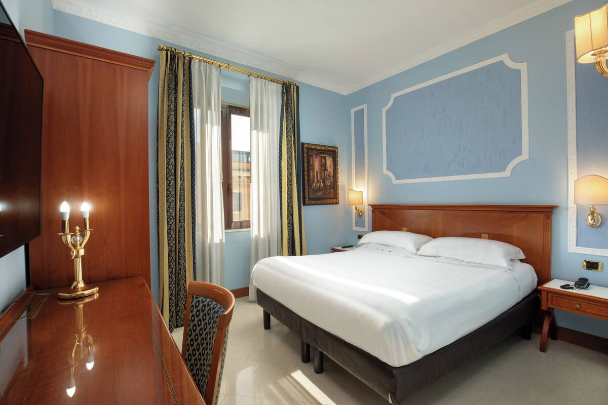 A hotel room with a wooden bed, a desk with a lamp, and a chair.