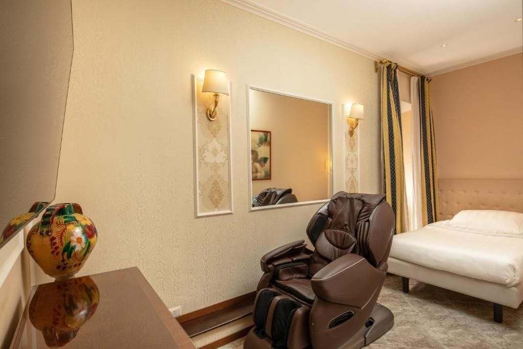 Habitación de hotel con sillón de masaje, cama y espejo.