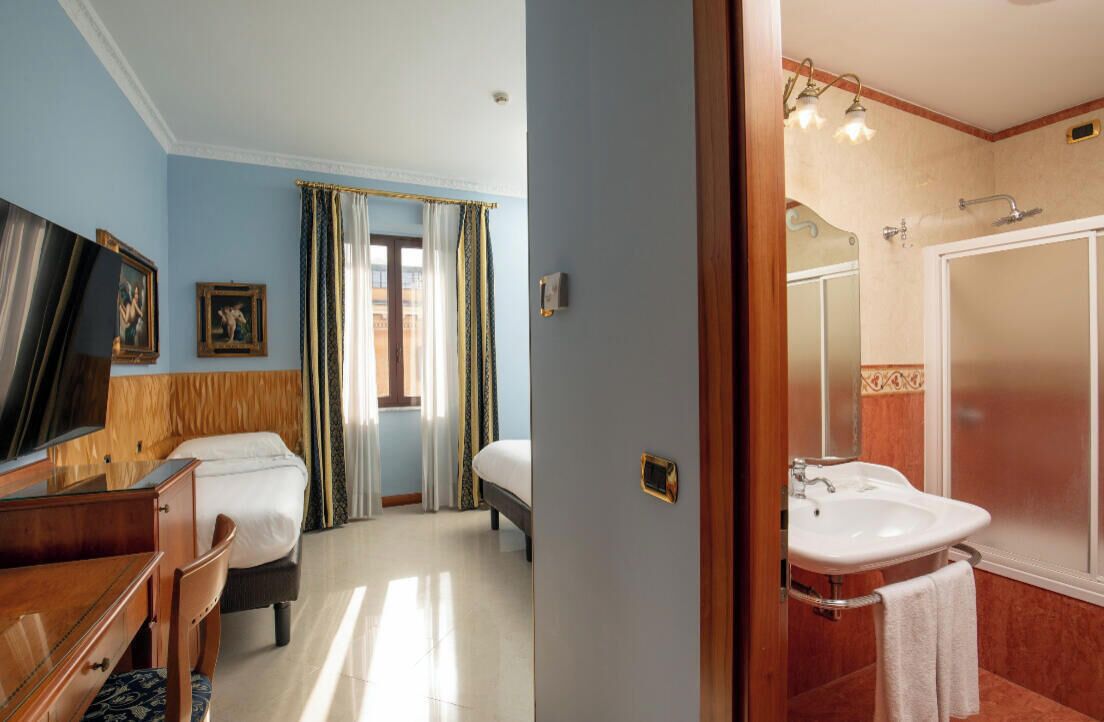 A hotel room with a bed, a desk, a chair, a TV, and a bathroom with a sink and shower.