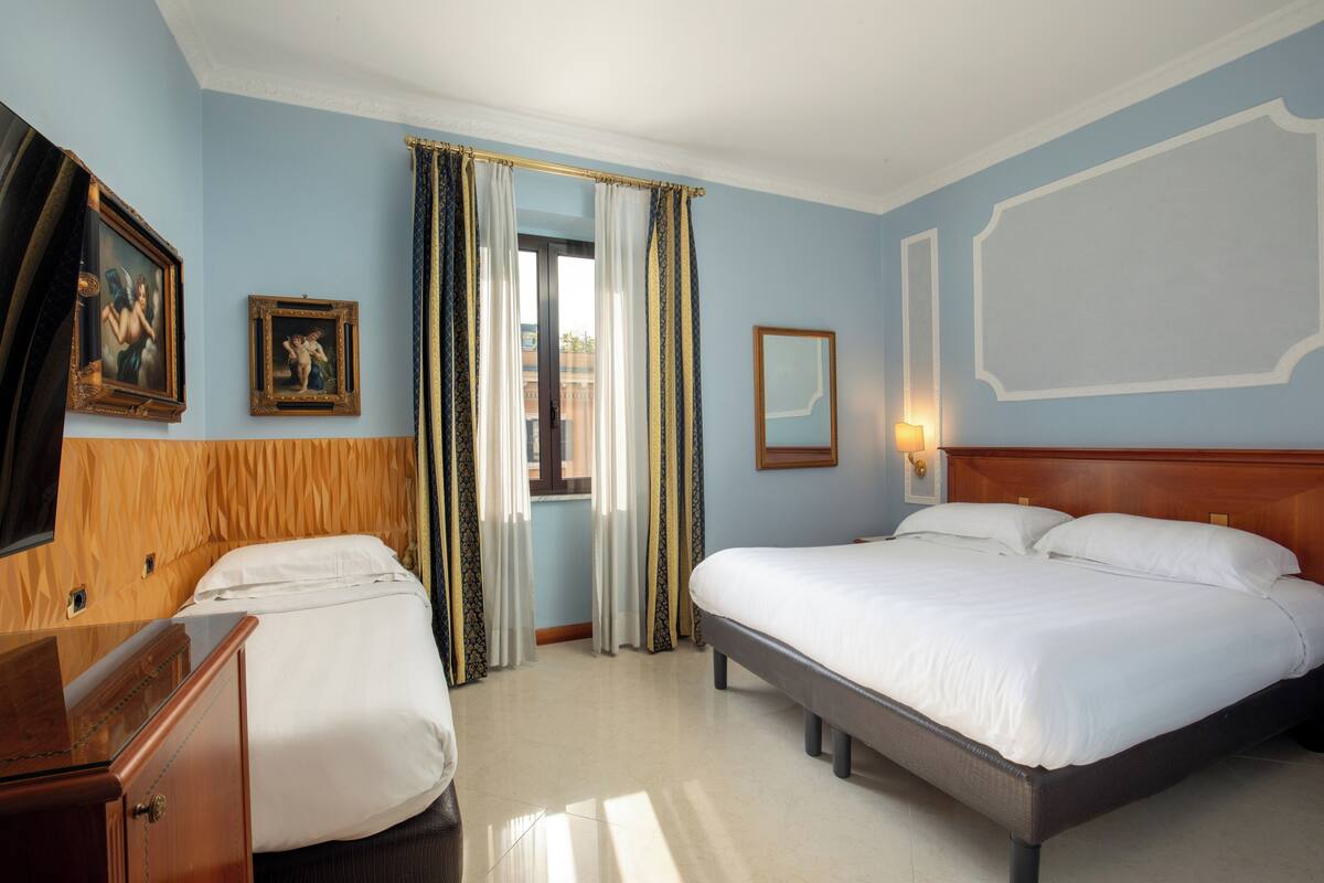 A hotel room with two beds, a wooden headboard, a nightstand, and a window with curtains.