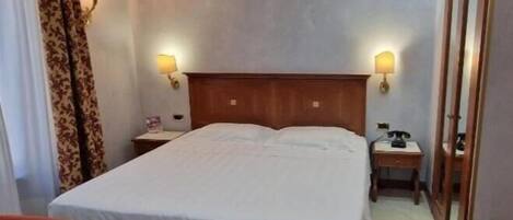 A hotel room with a large bed, two bedside tables, a wooden headboard, and two wall-mounted lamps.